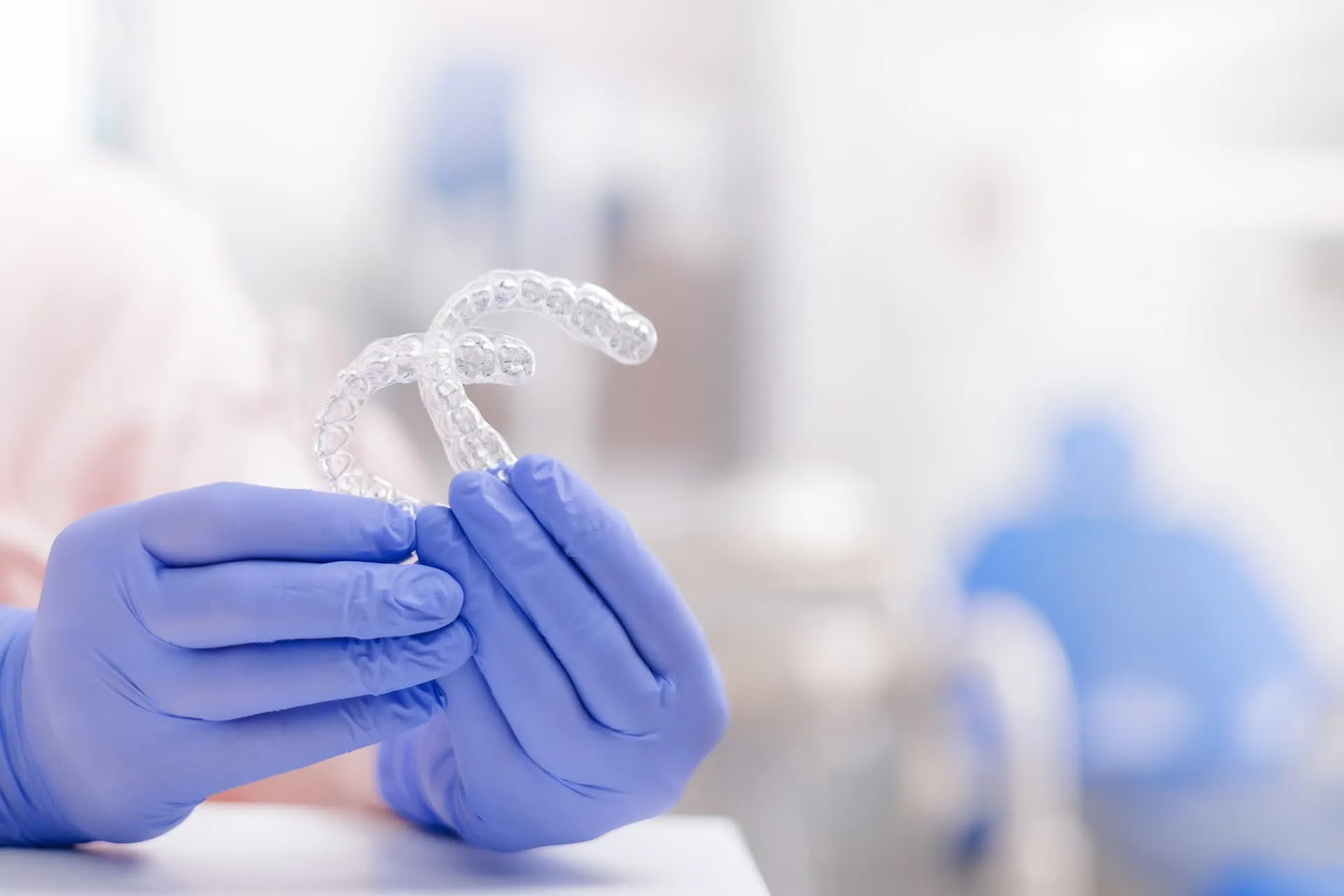 Mano con guante sujetando un alineador dental transparente de ortodoncia invisible